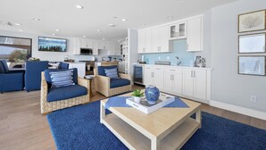 Een moderne woonkamer met een blauwe bank, een salontafel en een keuken met witte kasten en een blauwe spatwand.