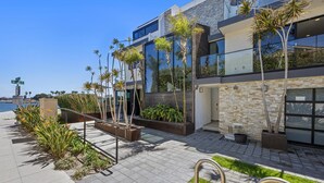 Een modern gebouw met grote glasramen, een stenen gevel en een aangelegde buitenruimte met palmboompjes en beplanting.
