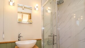 A bathroom with a white sink, a glass shower enclosure, and a mirror with lights. - Tawny (Crediton)