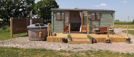 A small wooden cabin with a deck, a hot tub, and potted plants.