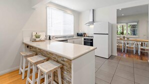 Eine moderne Küche mit Kochinsel, weißen Schränken, einem eingebauten Backofen und einem Essbereich mit Holztisch und weißen Stühlen.
