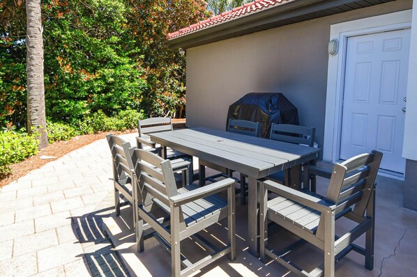 Un patio al aire libre con mesa y sillas, una parrilla de barbacoa y una puerta de garaje.