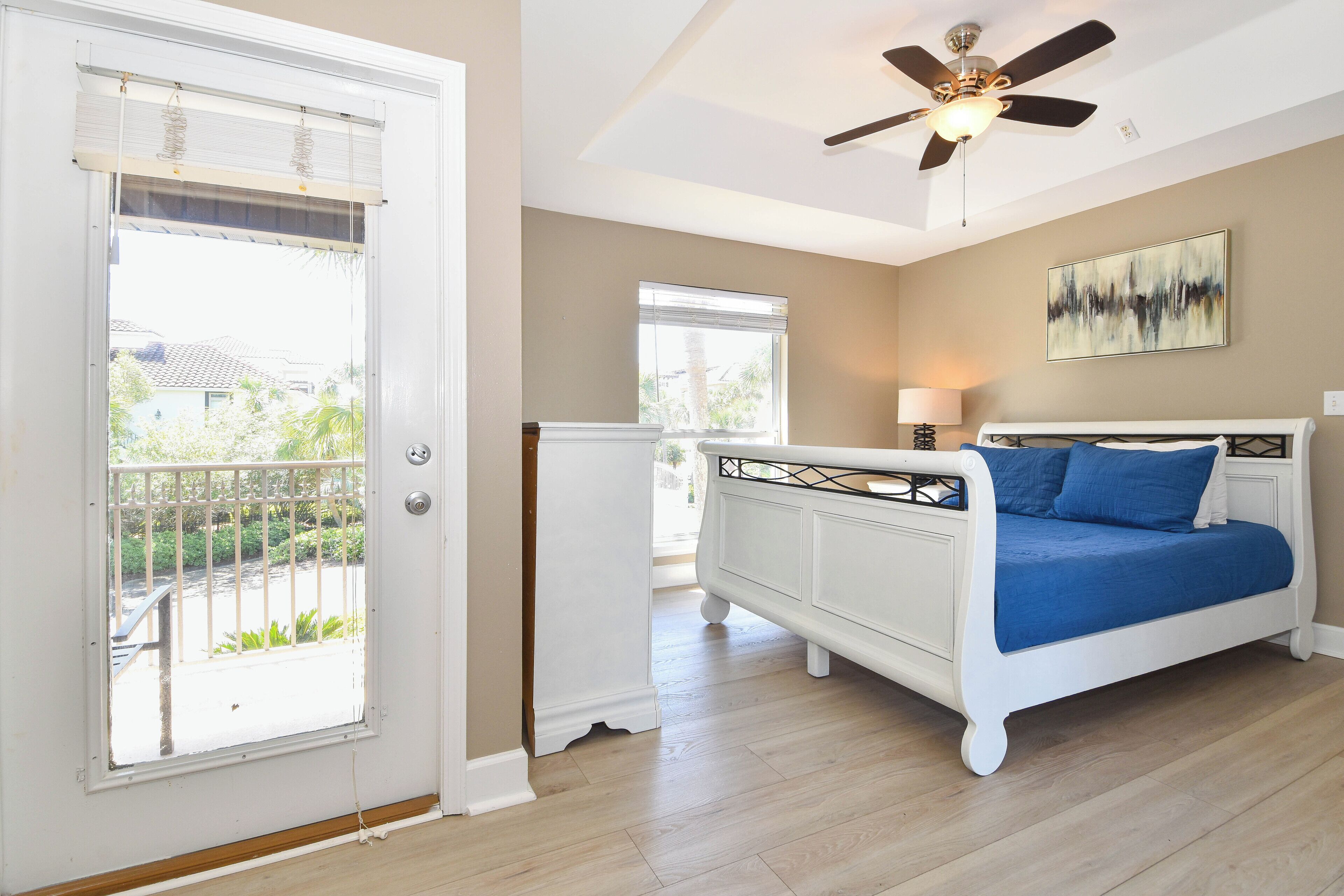A bedroom with a white bed, a ceiling fan, and a view of the outside.