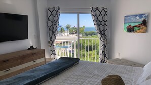 A bedroom with a bed, a wooden dresser, a TV, and a balcony with a view of the sea and palm trees. - Ocean Views at Ocean Pointe 
Tavernier, FL (Tavernier)