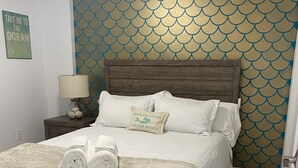 A neatly made bed with a quilted white cover, a wooden headboard, and a decorative pillow with a mermaid and starfish design. - Ocean Views at Ocean Pointe 
Tavernier, FL (Tavernier)
