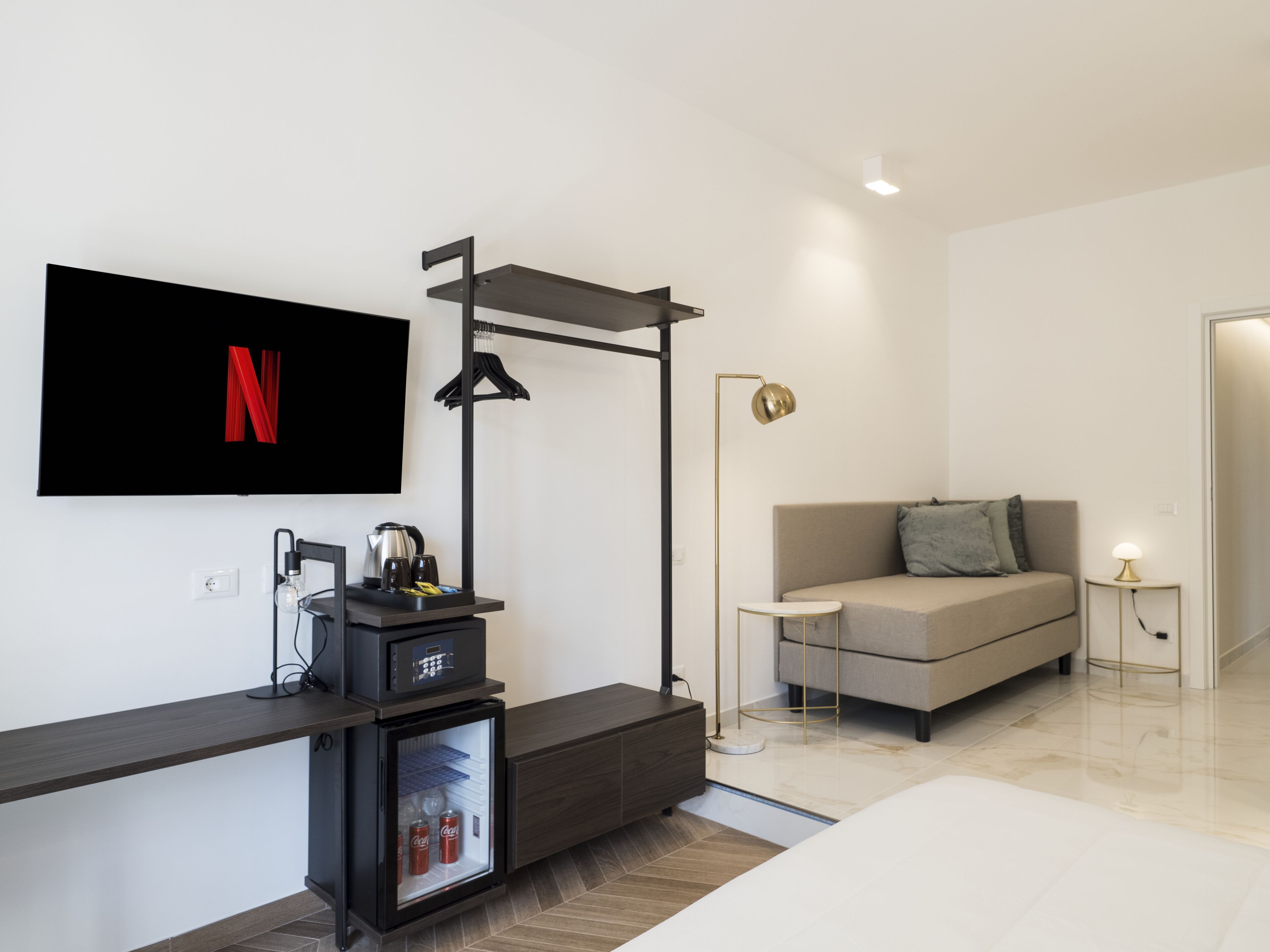 Una camera d'albergo moderna con televisore a schermo piatto montato a parete, un divano, un tavolino, una lampada da comodino e un minibar.
