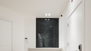 A hallway with a white reception desk, a black marble wall, and a wooden herringbone floor. - Savoia Rooms Roma (Rome)