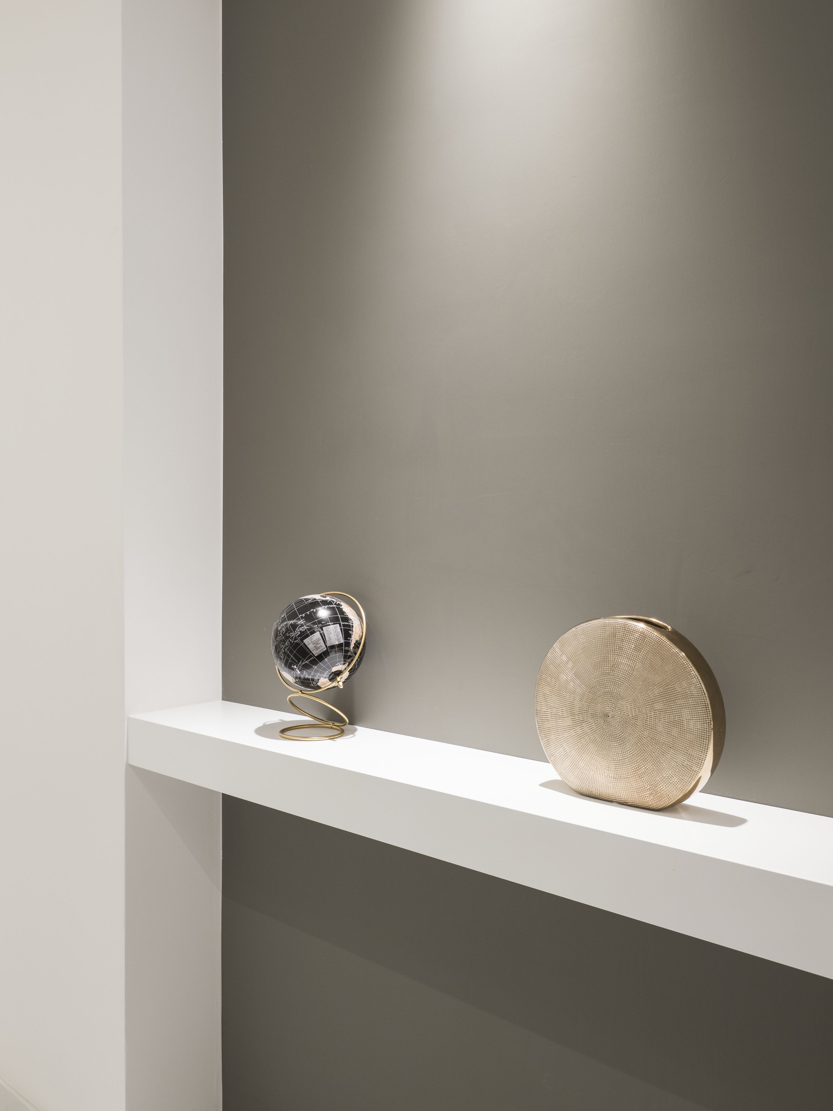 Una mensola dal design minimalista con due elementi decorativi: un globo riflettente e un piatto circolare con texture.