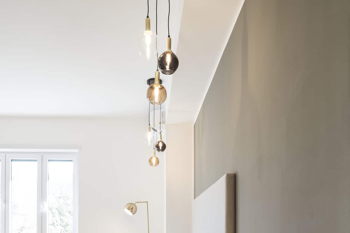 A modern bedroom with a bed, bedside table, lamp, and hanging pendant lights.