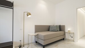 A modern, minimalist room with a sofa, a floor lamp, and a small table. - Savoia Rooms Roma (Rome)