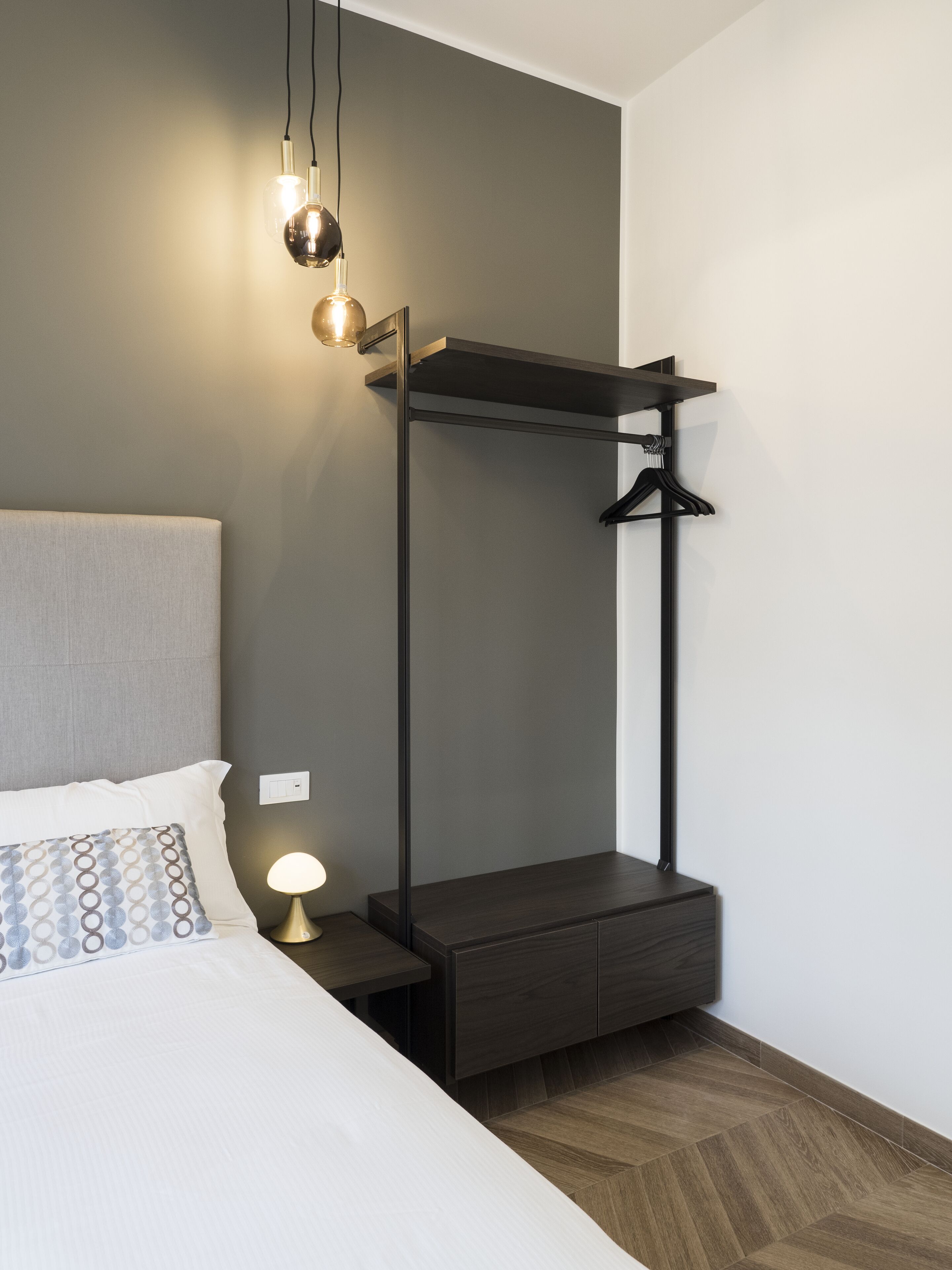 A modern bedroom with a bed, bedside lamp, and a built-in wardrobe with a hanging rack.
