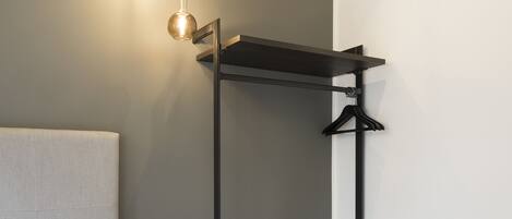 A modern bedroom with a bed, bedside lamp, and a built-in wardrobe with a hanging rack.