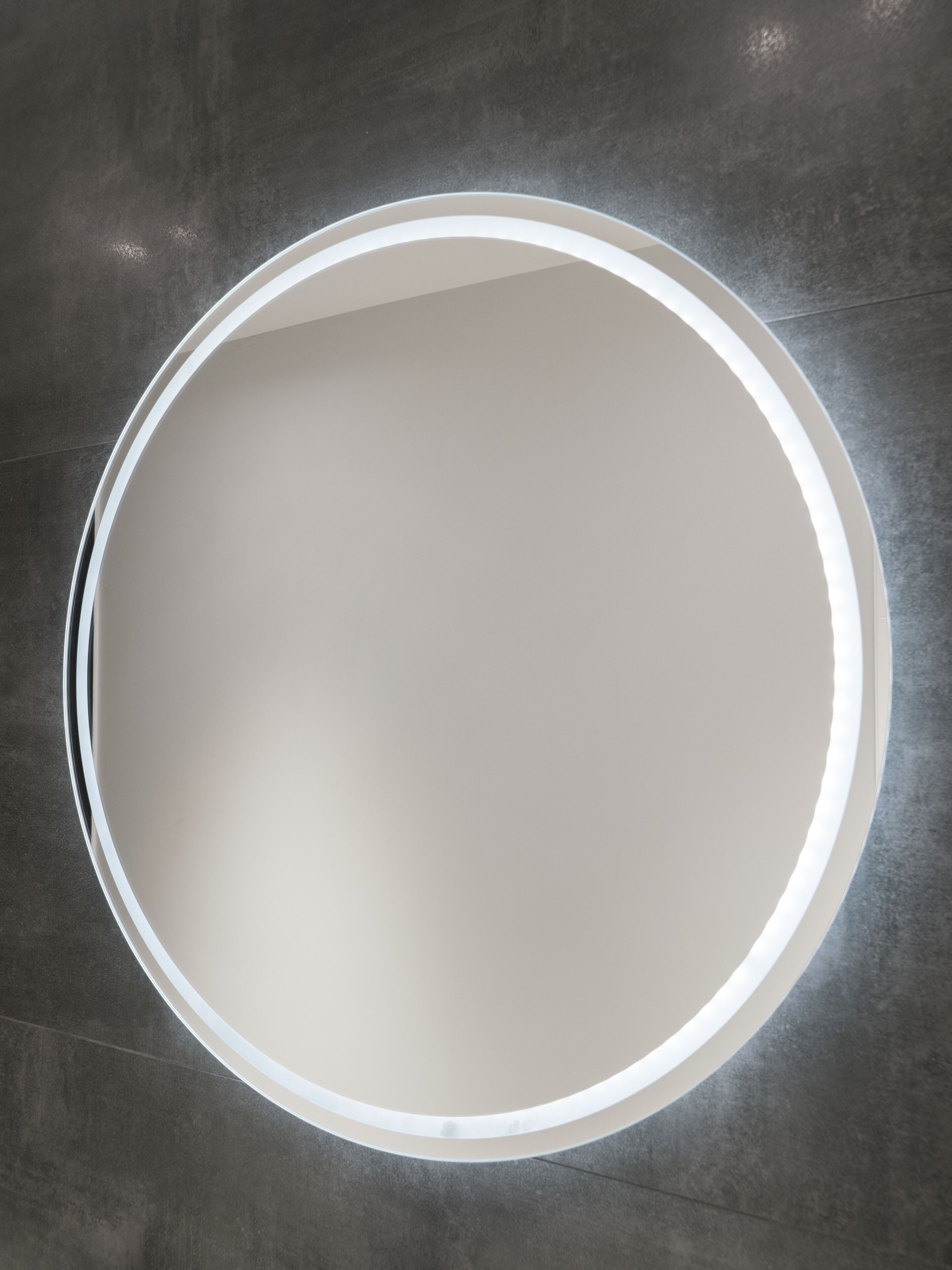 A circular mirror with a white frame on a textured grey wall.