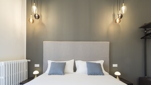 A neatly made bed with a grey headboard, two bedside lamps, and a white radiator. - Savoia Rooms Roma (Rome)