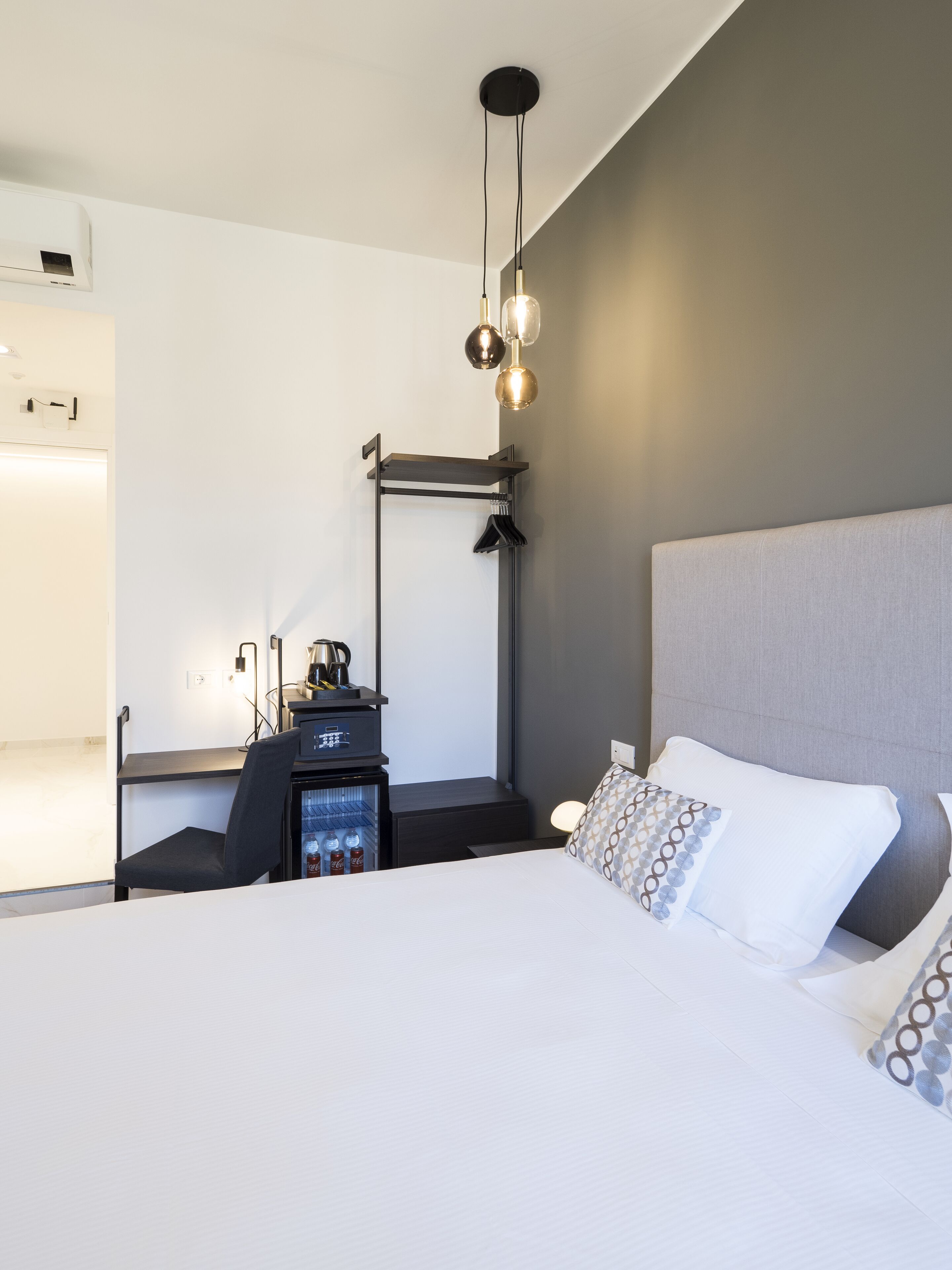 A modern hotel room with a bed, a desk with a coffee machine, and a minibar.