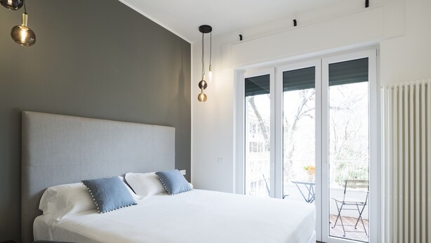 A modern bedroom with a large bed, a desk, and a view of the outdoors through a sliding glass door. - Savoia Rooms Roma (Rome)