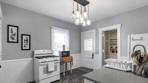 A compact kitchen with white appliances, a built-in microwave, and a hanging light fixture. - Kent Family Home | Walk to Downtown + Pet Friendly (Kent)
