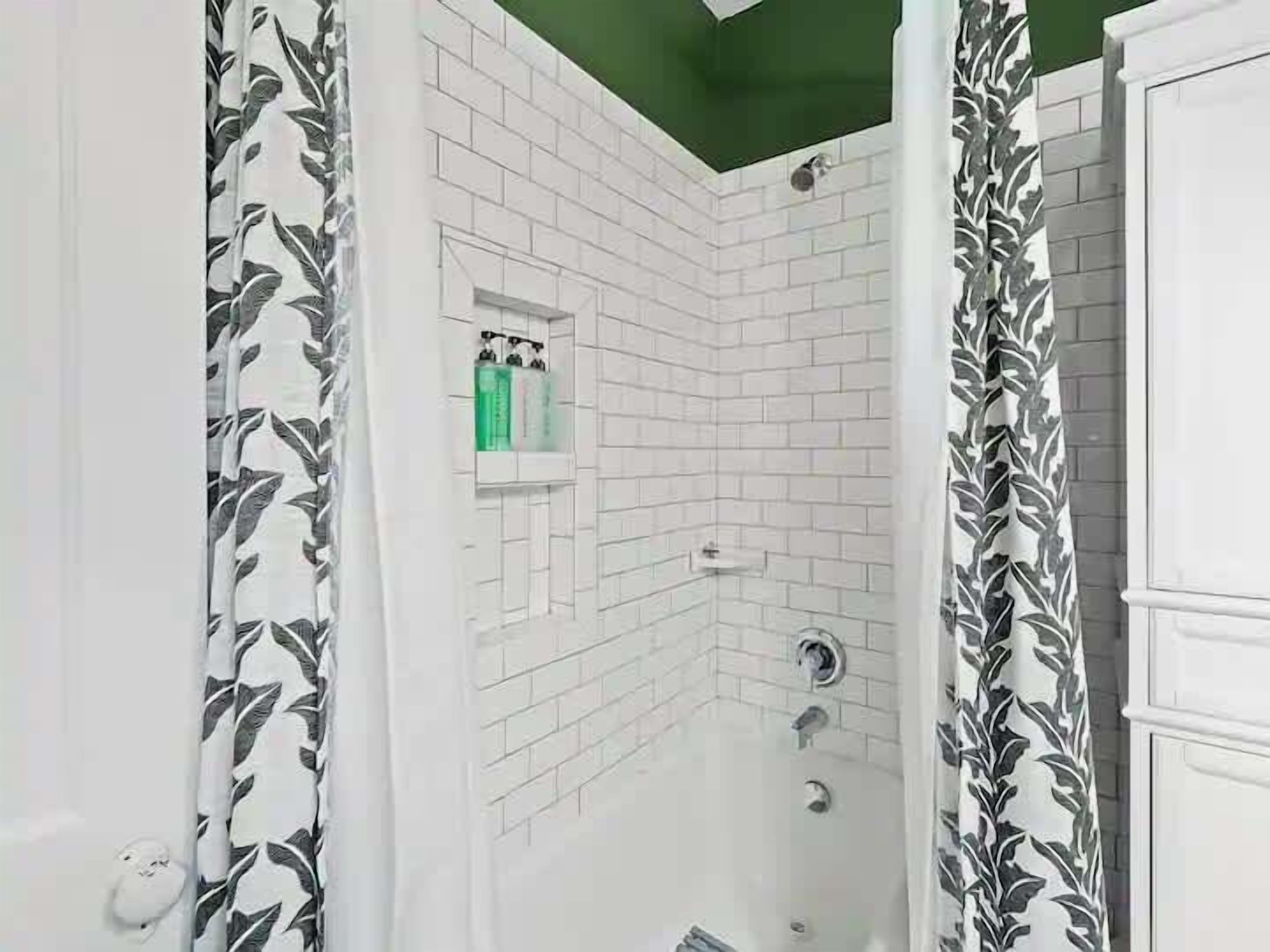 A bathroom with white tiled walls, a shower, and a green-tiled niche with toiletries.