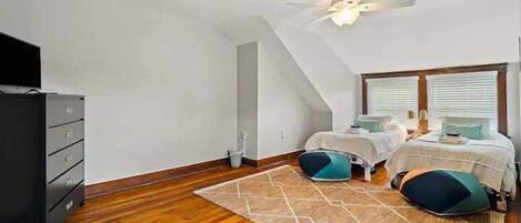 Un dormitorio con techo inclinado, ventilador de techo, cama con dos almohadas, cómoda y ventana con persianas.