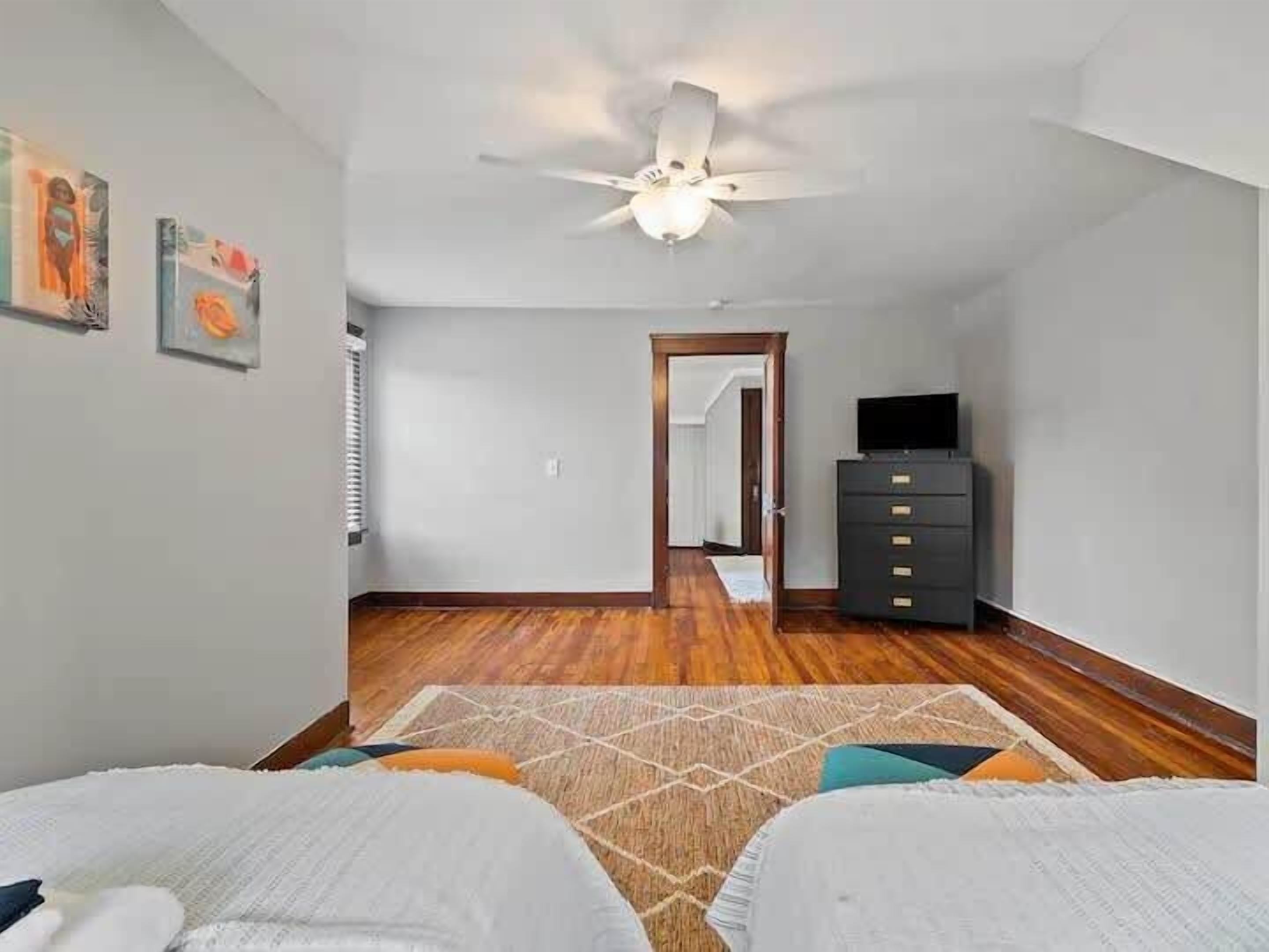 A bedroom with two beds, a ceiling fan, a dresser, and a television.