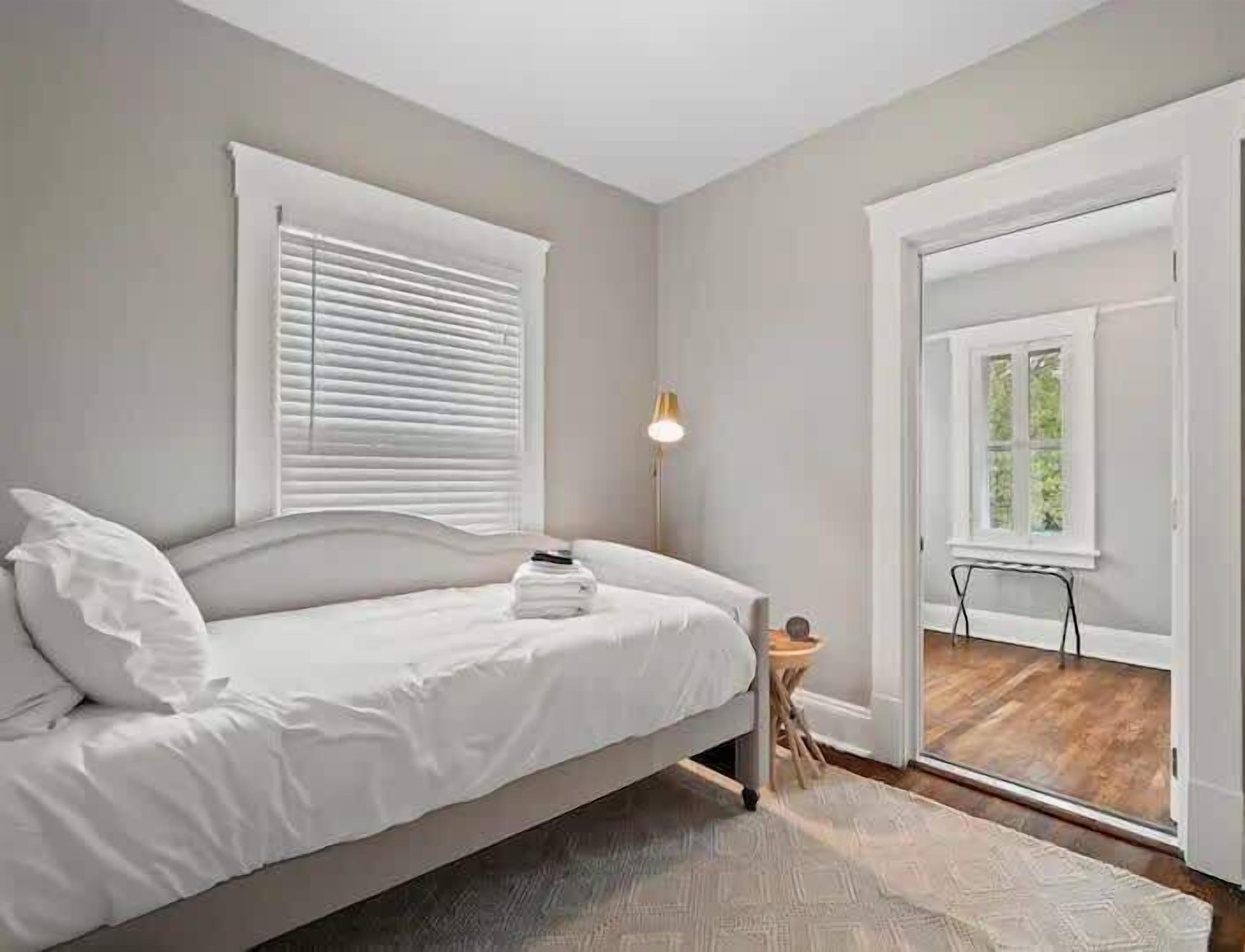 A bedroom with a bed, a bedside table, a lamp, and a view of the outdoors through a door.
