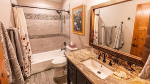 Un baño con bañera, inodoro, lavamanos y un espejo grande.
