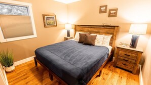 Un dormitorio con una cama de madera, dos mesitas de noche con lámparas, una ventana con persianas y un cuadro en la pared.