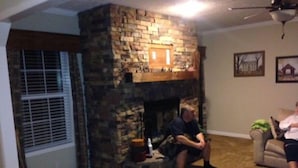 A living room with a stone fireplace, a window with blinds, and a ceiling fan. - motor home (Columbia)