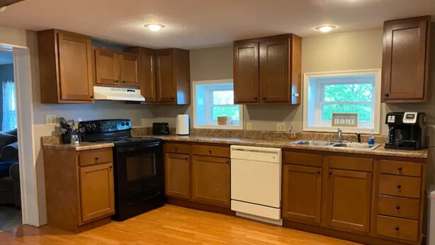 A kitchen with wooden cabinets, a black stove, a white dishwasher, and a window with a view of greenery. - The Old Farmhouse. (Dry Ridge)