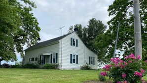 A white two-story house with a sloped roof, a chimney, and a small porch. - The Old Farmhouse. (Dry Ridge)