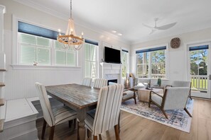 A dining room with a wooden table and striped chairs, a chandelier, and a fireplace. - Bonito Bliss - Golf Cart Included! 722 Bonito (Fripp Island)