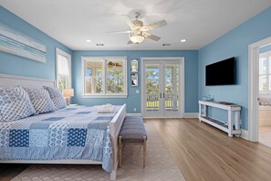 Une chambre à coucher comprenant un lit, un ventilateur de plafond, une fenêtre et une porte donnant sur un espace extérieur.