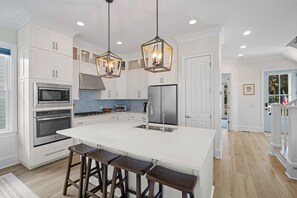 Une cuisine moderne avec des meubles blancs, des appareils en acier inoxydable et un îlot central doté de tabourets de bar.