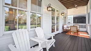 Varanda coberta com cadeiras Adirondack, deck de madeira e vista para o quintal.
