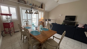A dining area with a wooden table, chairs, and a red cart. There is a ceiling fan and a TV in the living area. - Brigantine dream home just steps to the beach! (Brigantine)