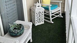 A small porch with a white rocking chair, a small table, and a wicker bench. - Brigantine dream home just steps to the beach! (Brigantine)