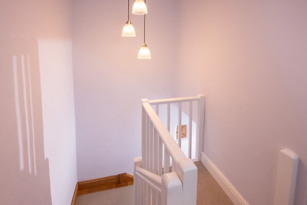 A staircase with white railings and a carpeted floor leading to a door. - 1 Bridge Syke, Elterwater (Ambleside)