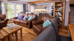 A cozy living room with leather sofas, a wooden coffee table, and a bookshelf filled with books. - 1 Bridge Syke, Elterwater (Ambleside)