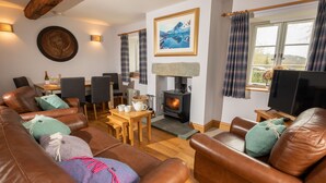 A cozy living room with leather sofas, a fireplace, a dining area, and a television. - 1 Bridge Syke, Elterwater (Ambleside)