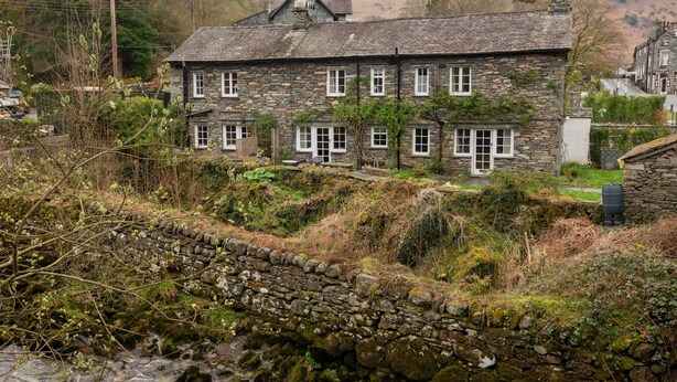 A stone house with multiple windows and a stone wall in the foreground. - 1 Bridge Syke, Elterwater (Ambleside)