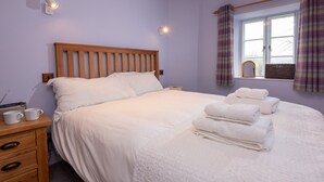 A neatly made bed with white linens, a wooden headboard, and a bedside table with a radio and two cups. - 1 Bridge Syke, Elterwater (Ambleside)