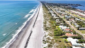 Luftaufnahme einer Küstenstadt mit langem Strand, Wohnhäusern und einem Yachthafen.