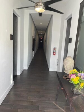 Ein Flur mit Deckenventilator, Feuerlöscher und einer Blumenvase auf einer Konsole.