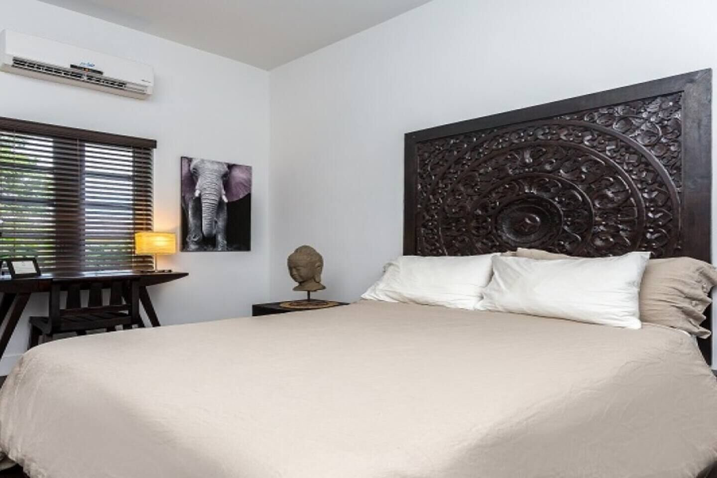 Un dormitorio con una cama grande, cabecera de madera, un escritorio con lámpara y aire acondicionado de pared.