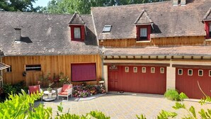 Una casa de madera con puerta de garaje roja, una ventana pequeña y un patio con baldosas y mobiliario exterior.