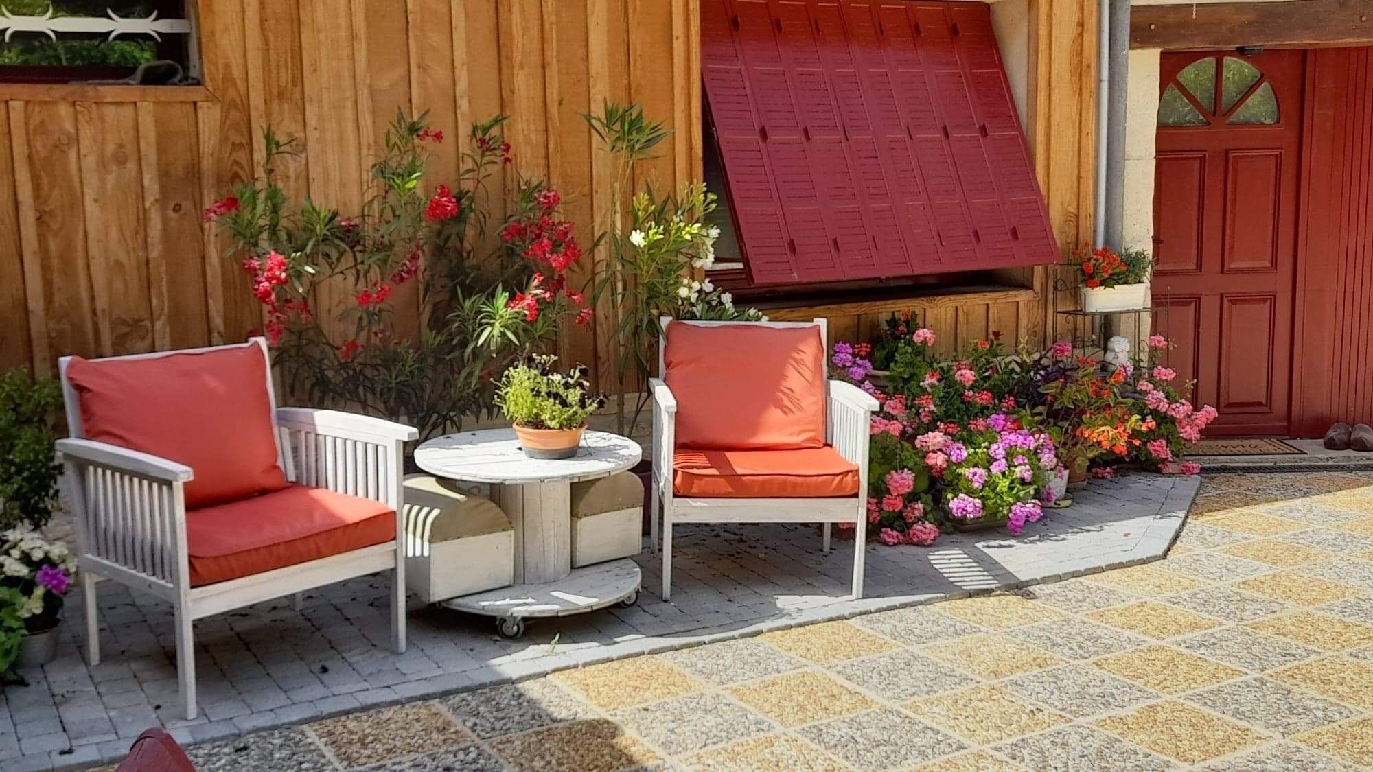 A patio with two white chairs and a small table, surrounded by potted plants and flowers.