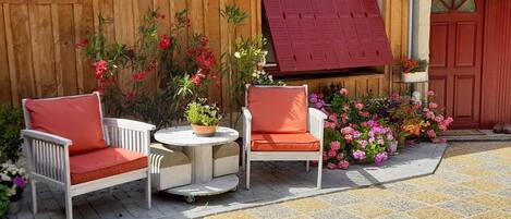 A patio with two white chairs and a small table, surrounded by potted plants and flowers.