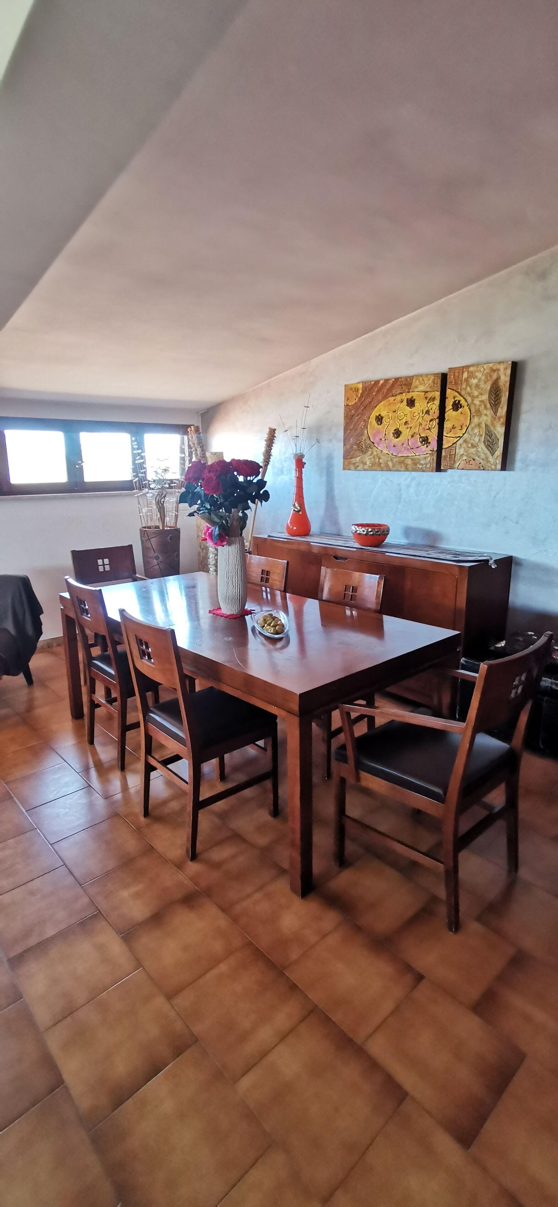 Un coin repas avec une table et des chaises en bois, un vase de fleurs et deux tableaux accrochés au mur.