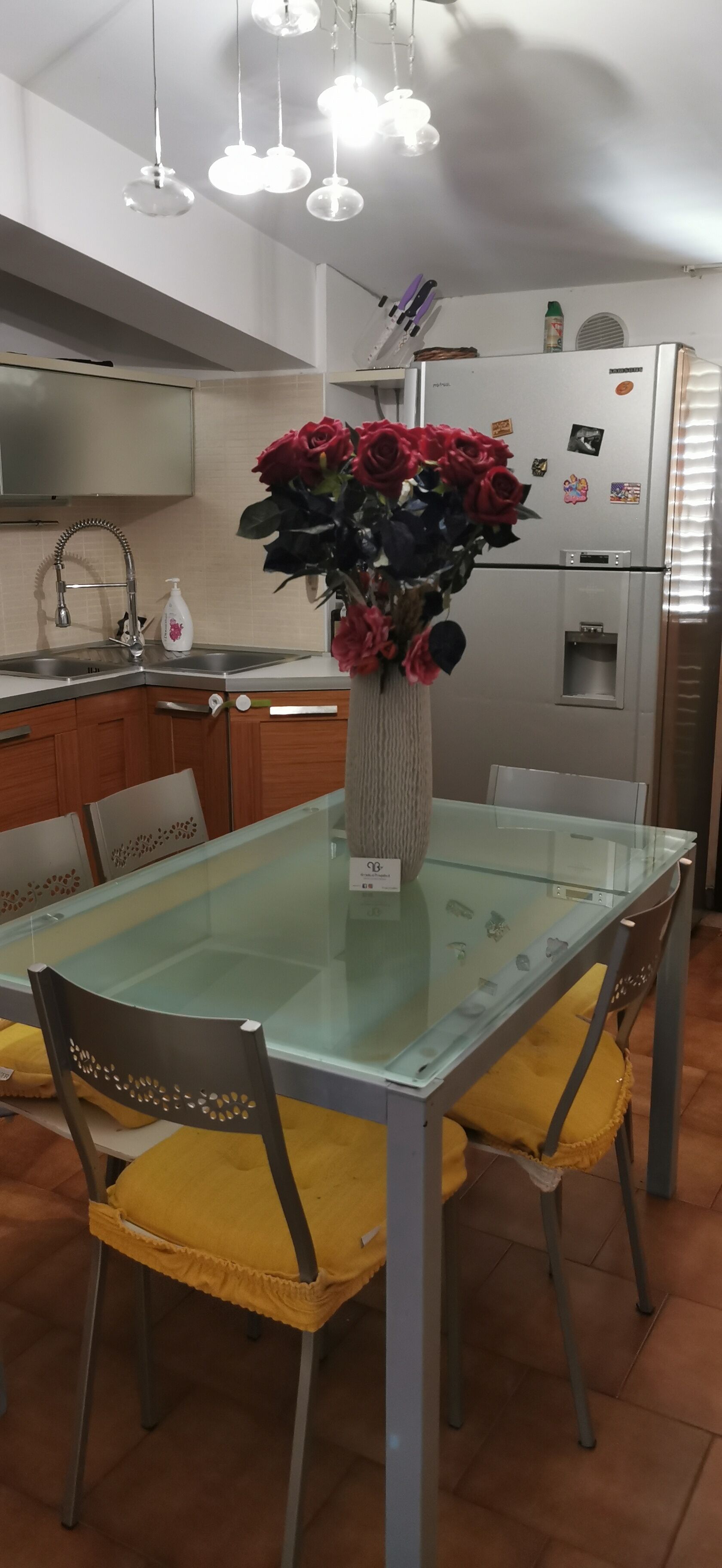 Een moderne keuken met een glazen eettafel, gele stoelen en een vaas rode rozen.