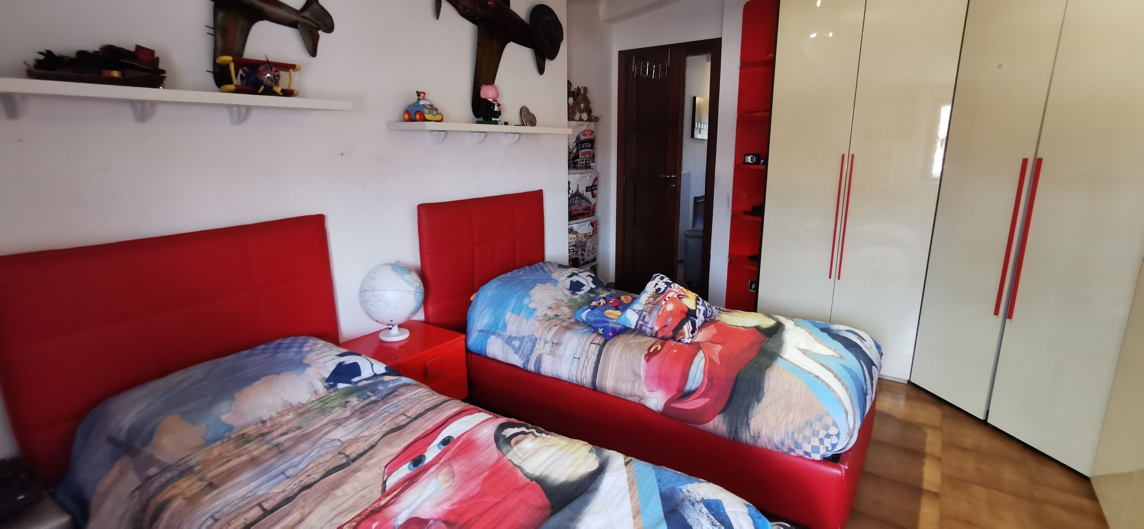 Un dormitorio con dos camas, cada una con cabecero rojo, y un armario con pomos rojos.